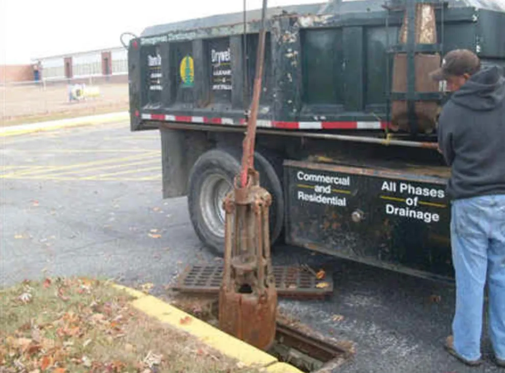 Evergreen technician cleaning a parking-lot catch basin next to a dump truck lettered Commercial and Residential, All Phases of Drainage